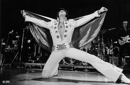 Elvis Presley singing on stage in white outfit
