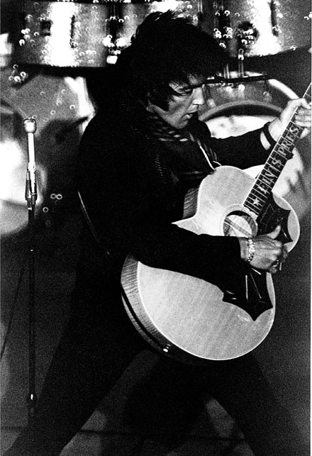 Elvis Presley wearing black outfit and playing guitar
